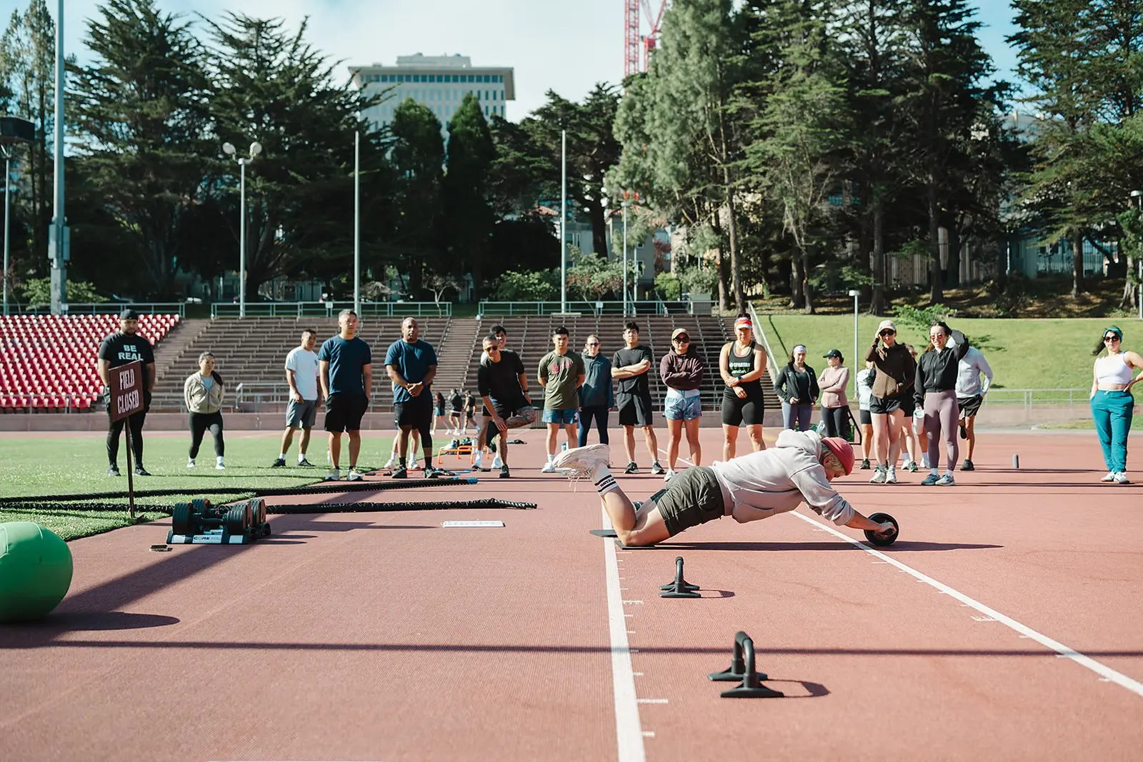 Coach demonstrating an ab wheel rollout while the bootcamp group watches on the track