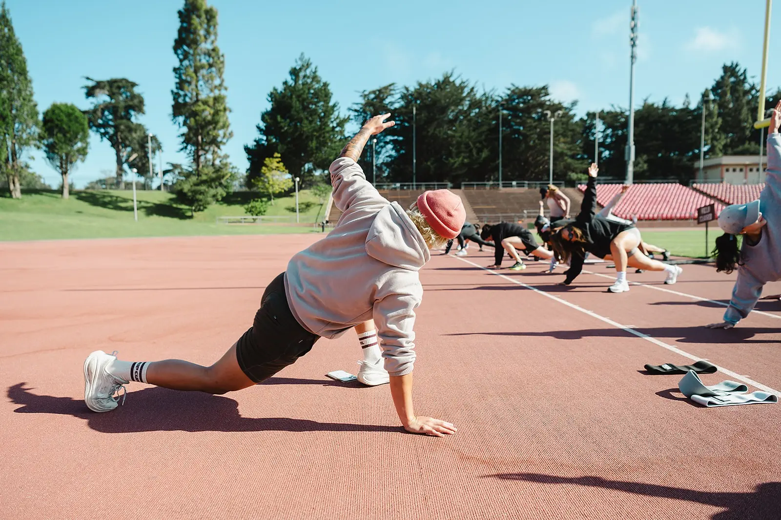 Coach leading a mobility lunge stretch with the group lined up on the track