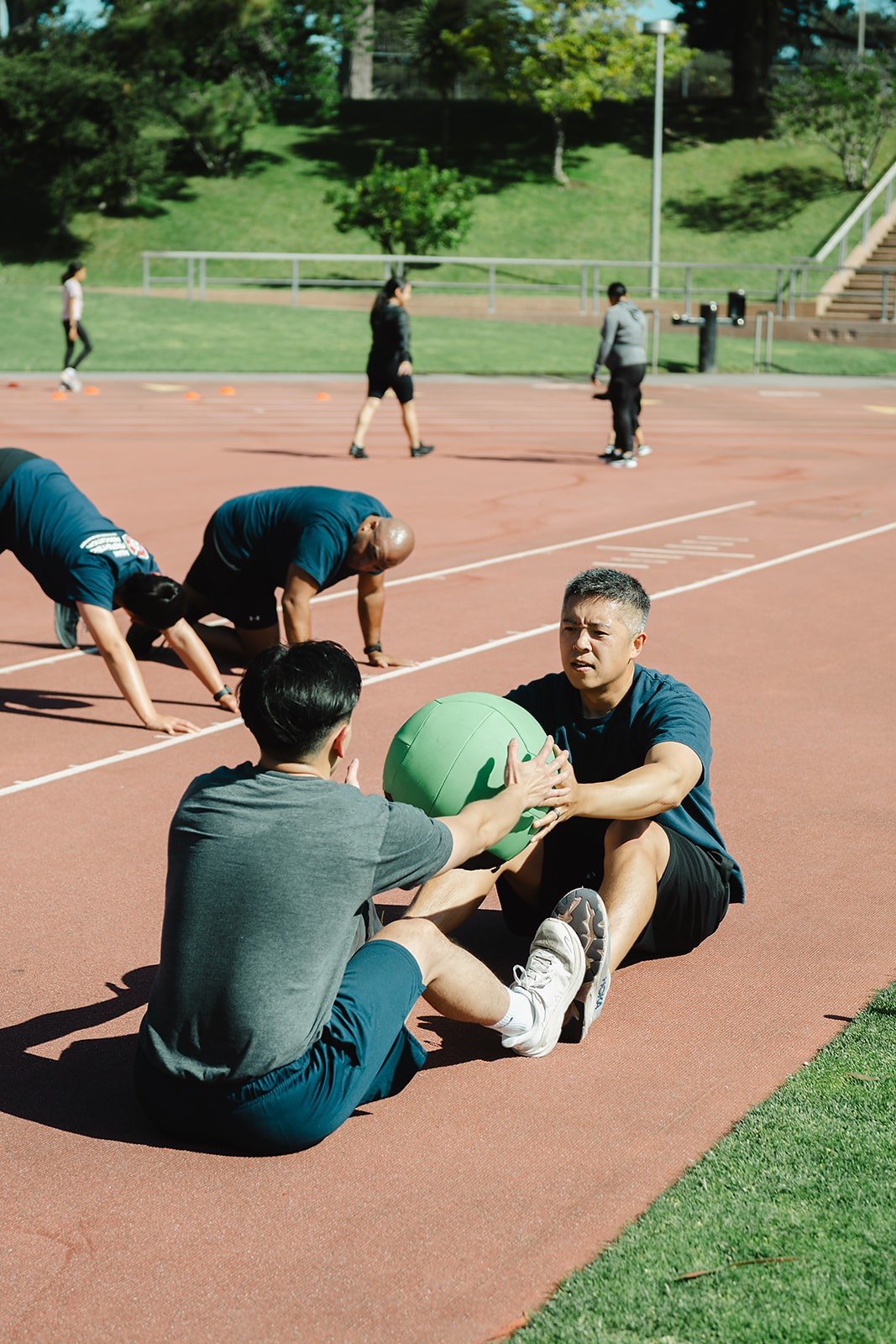 Two members passing a medicine ball during a partner core drill on the track